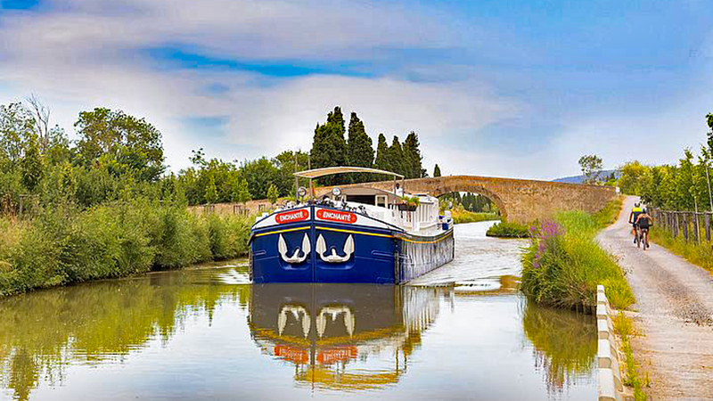 French Hotel Barge Enchante cruising the canal du midi with cyclists on the towpath