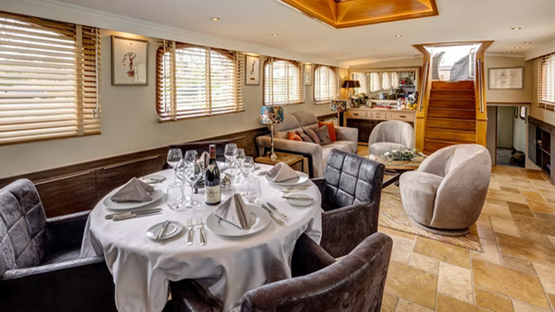French Hotel Barge Rendez-Vous - This photo shows the set Dining table with the seating area, bar and entrance behind